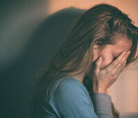 Depressed woman with long hair covering her face with hands, sitting alone in dim lighting, showing signs of emotional distress