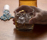 Glass of alcohol with ice cubes next to spilled antibiotic pills, illustrating the risks of combining alcohol and antibiotics