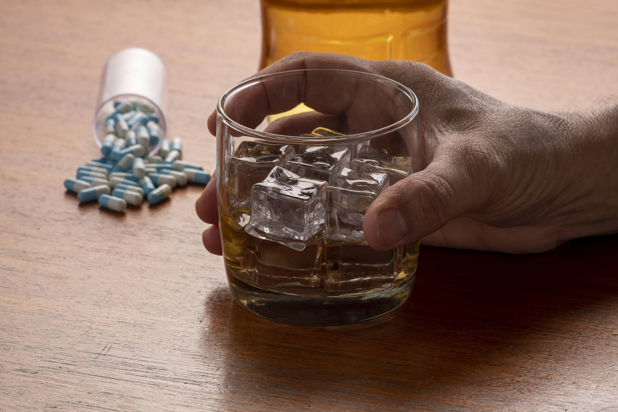 Glass of alcohol with ice cubes next to spilled antibiotic pills, illustrating the risks of combining alcohol and antibiotics