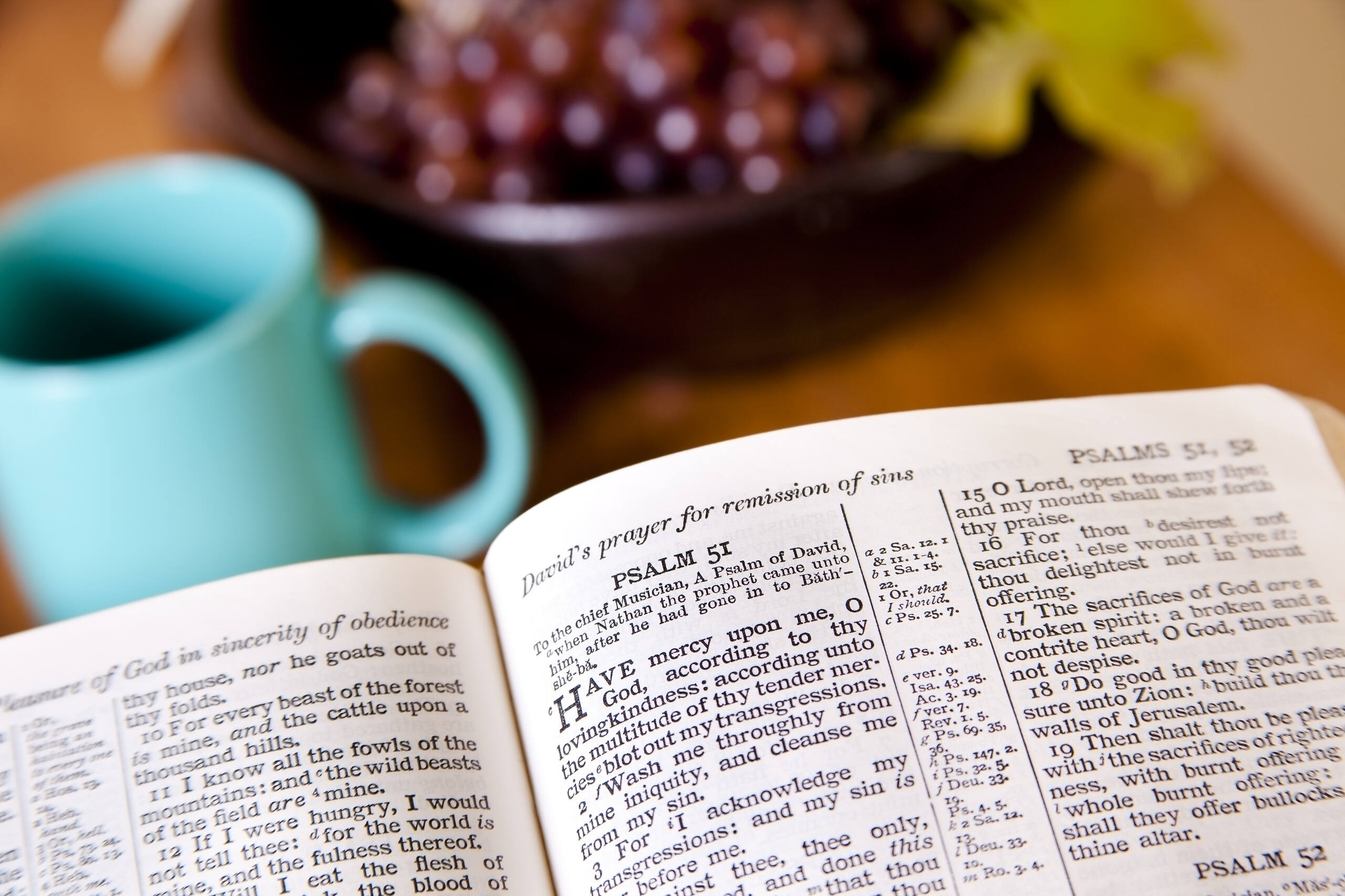 Open Bible showing Psalm 51, David's prayer for forgiveness, with a teal coffee mug and grapes in the background, illustrating spiritual reflection in Christian rehab