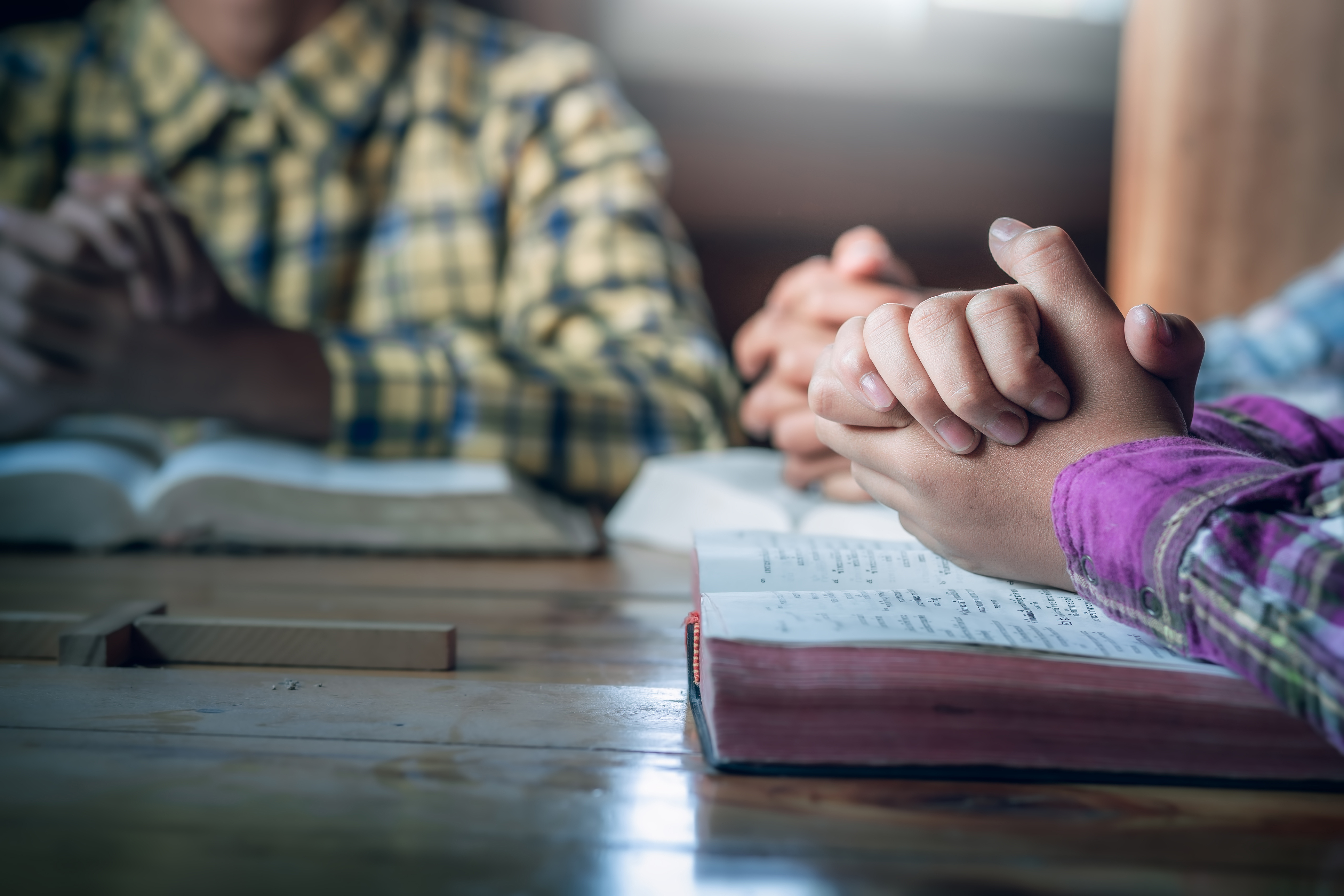 Two people holding hands in prayer over open Bibles during a Christian addiction recovery session