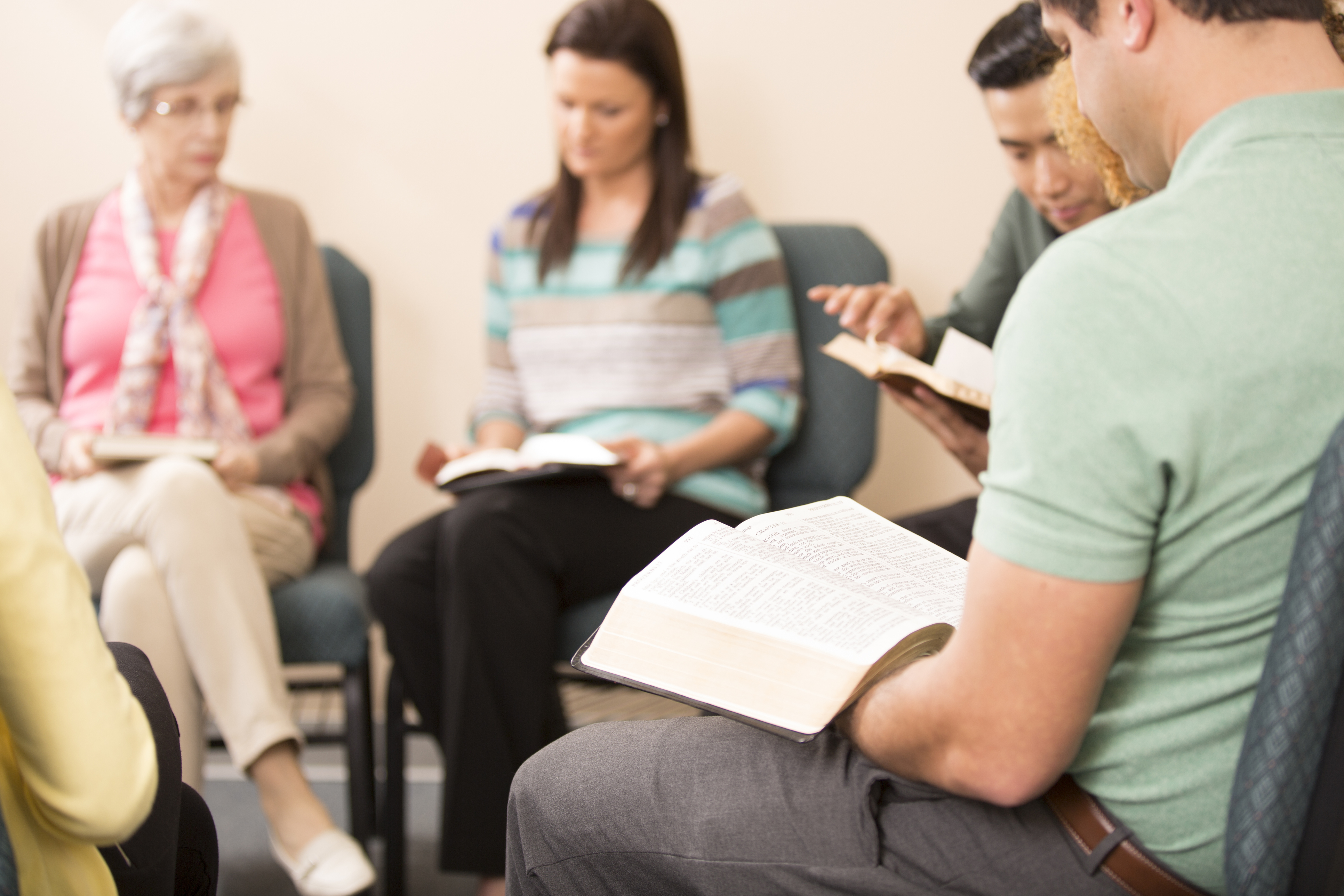 Diverse group of people participating in a Christian rehab support meeting, reading from books, likely Bibles or recovery materials