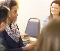 Multi-ethnic group of adults in a supportive counseling session, with a young African American woman speaking to attentive participants.