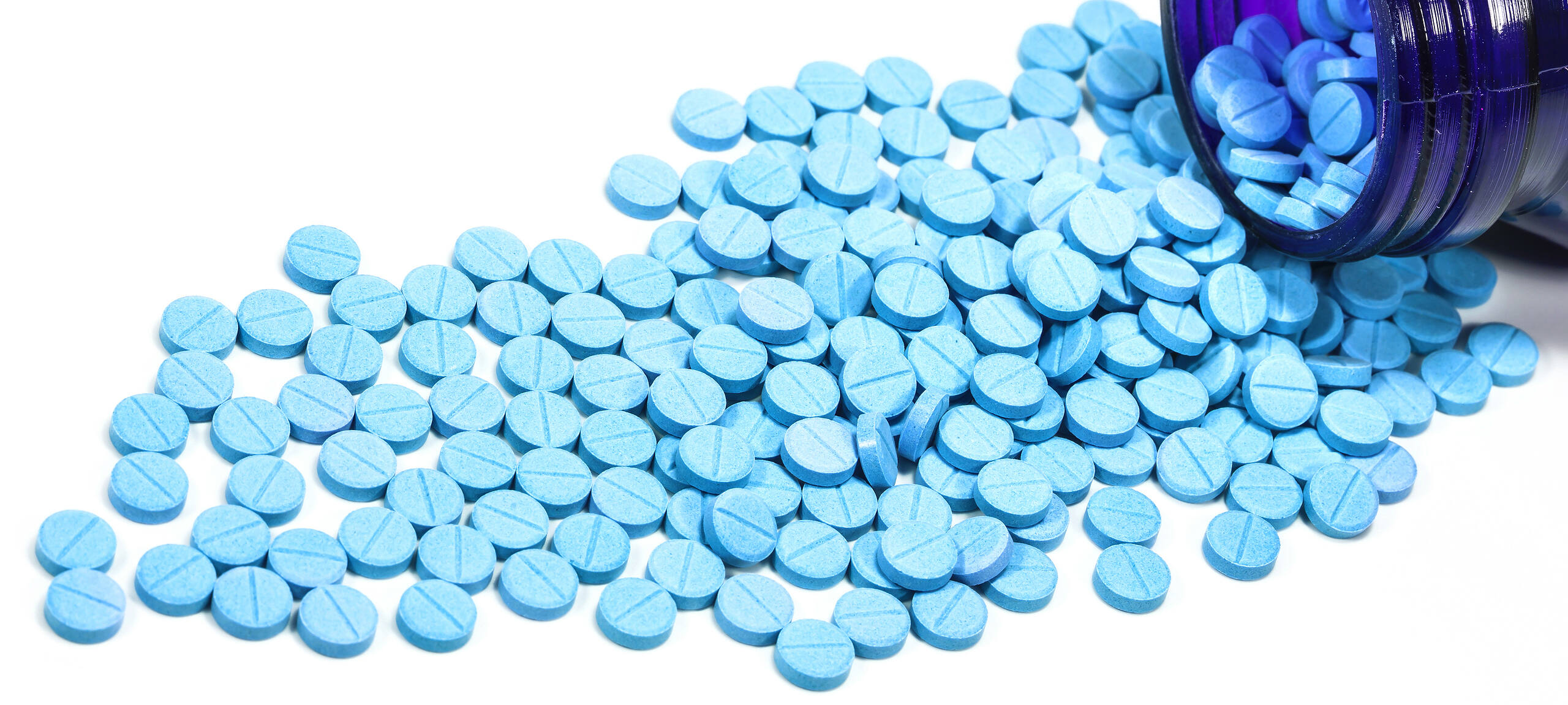 Blue Klonopin (Clonazepam) pills scattered from an open prescription bottle on a white background