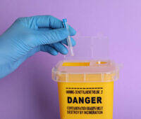 Gloved hand placing a syringe into a yellow sharps container labeled 'DANGER' against a purple background, highlighting safe disposal practices in addiction treatment