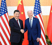 Two men in suits shaking hands: US President Joe Biden and Chinese President Xi Jinping standing in front of American and Chinese flags during a diplomatic meeting