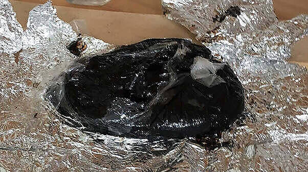 Close-up image of black tar heroin, a dark, sticky substance, partially wrapped in aluminum foil, illustrating the dangerous drug's appearance