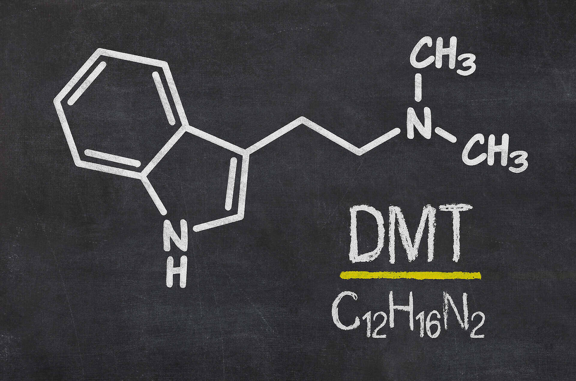 Chemical structure of DMT (Dimethyltryptamine) drawn in chalk on a blackboard, showing molecular formula C12H16N2