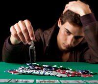 Man holding his head in distress while reaching for poker chips, illustrating gambling addiction