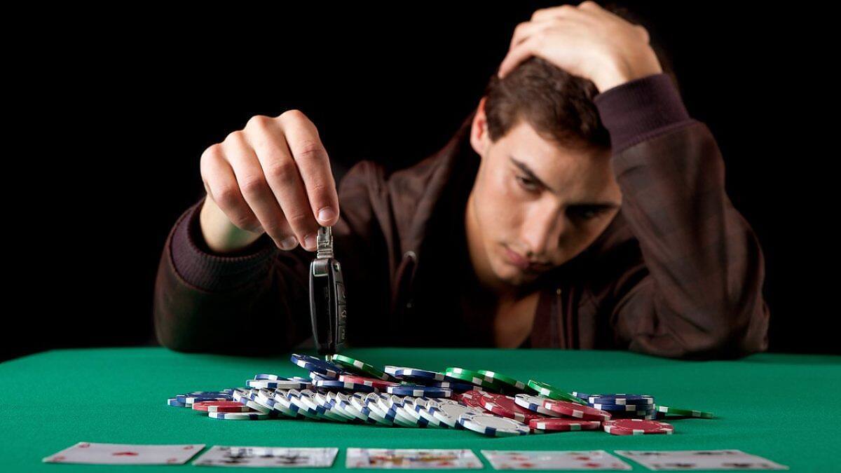 Man holding his head in distress while reaching for poker chips, illustrating gambling addiction