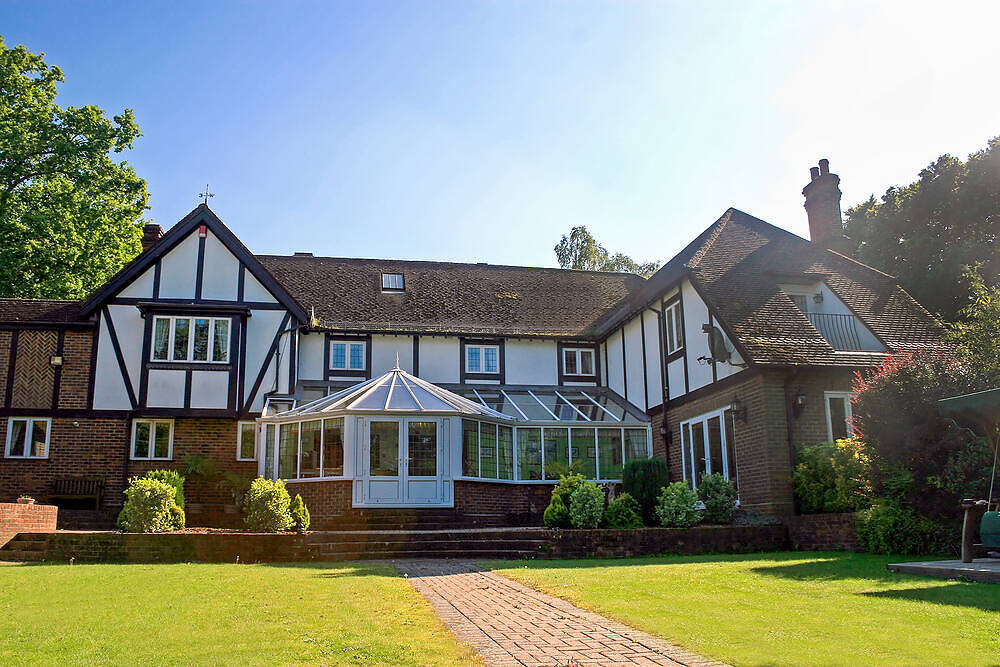Exterior view of a Tudor-style building with a glass conservatory, surrounded by well-maintained gardens and trees