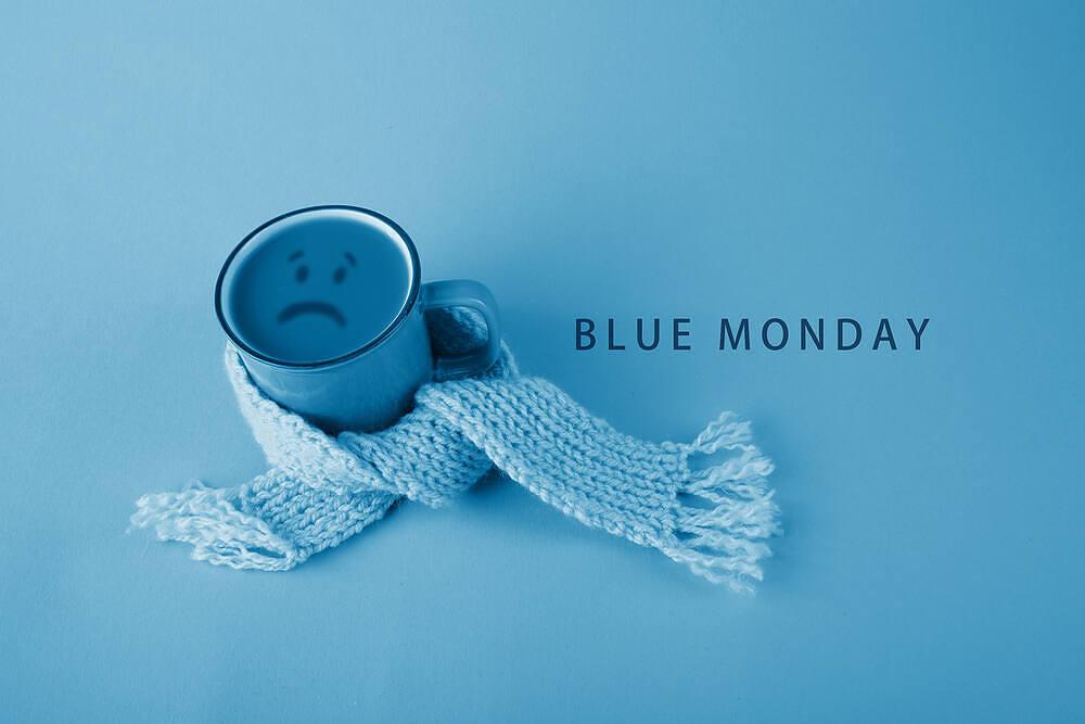 Blue mug with sad face wrapped in light blue scarf, representing Blue Monday and seasonal depression