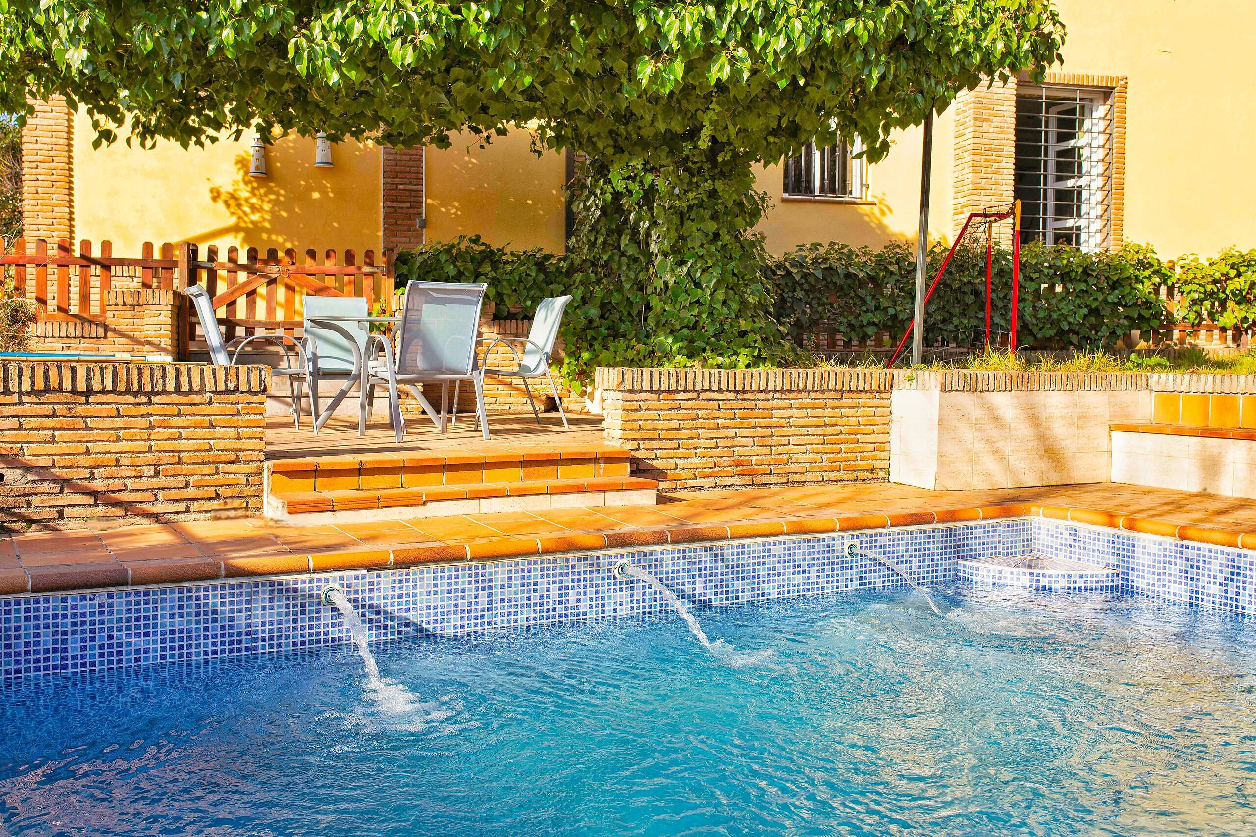 Inviting pool area of a Spanish rehab center with comfortable seating, lush greenery, and a sunny yellow villa backdrop