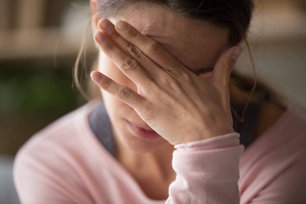 Young woman in pink sweater covering her face with her hand, showing signs of fatigue and distress potentially related to Adderall addiction