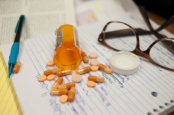 Spilled Adderall pills from prescription bottle next to glasses and notepad, illustrating addiction and treatment