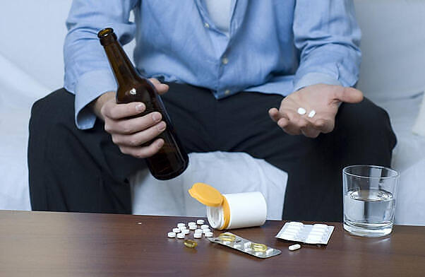 Man holding beer bottle and pills, depicting risky combination of alcohol and medications like naproxen