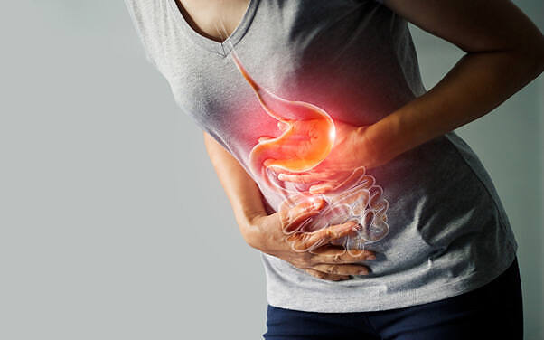 Person clutching stomach in pain with highlighted digestive system, illustrating potential gastrointestinal effects of combining naproxen and alcohol