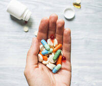 Hand holding assorted colorful prescription pills and capsules, with medication bottle in background
