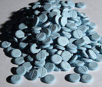 Close-up image of a large pile of light blue prescription pills, likely opioids, scattered on a white surface, illustrating the scale of prescription drug abuse