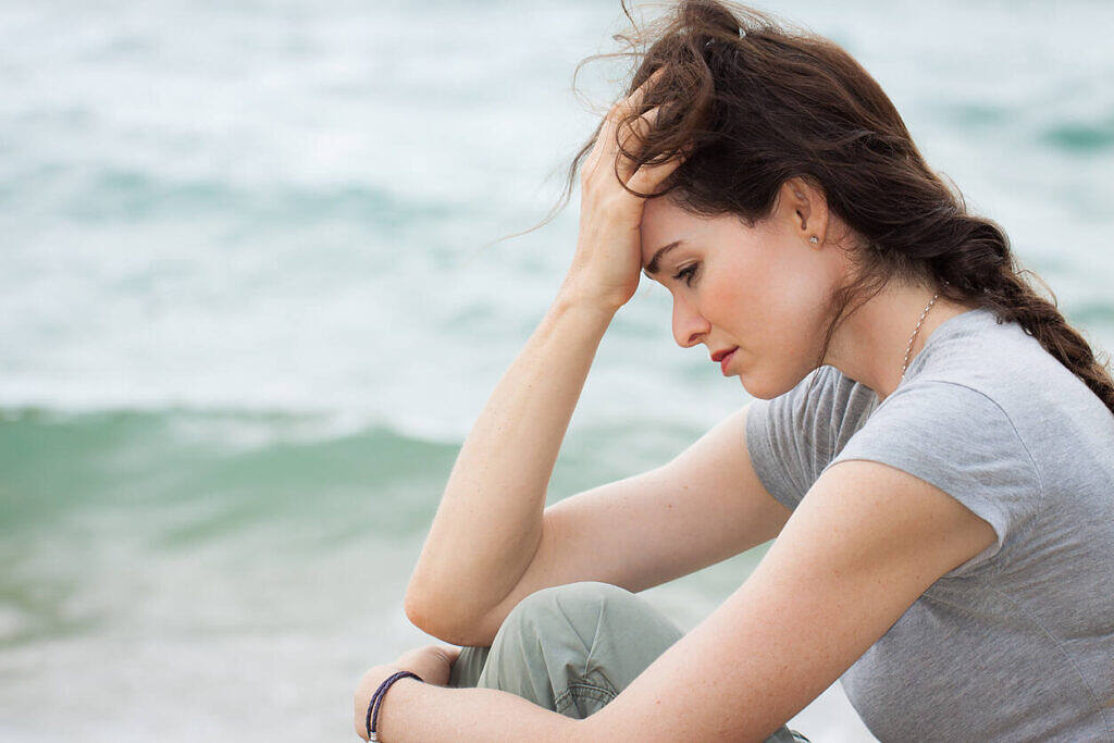 Close-up of a sad and depressed woman sitting by the beach, reflecting on her drug detox journey.