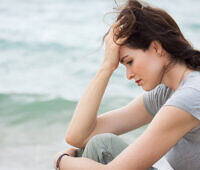Close-up of a sad and depressed woman sitting by the beach, reflecting on her drug detox journey.
