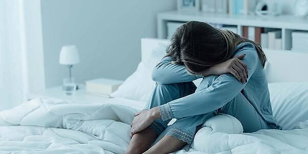 Distressed woman sitting on bed, hugging knees, head down, depicting insomnia and potential zopiclone addiction side effects