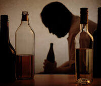 A silhouette of a man sitting with bottles of alcohol, symbolizing the challenges of alcohol addiction.