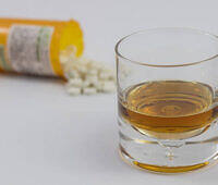 Glass of alcohol next to spilled prescription pills, illustrating risks of combining alcohol with medications