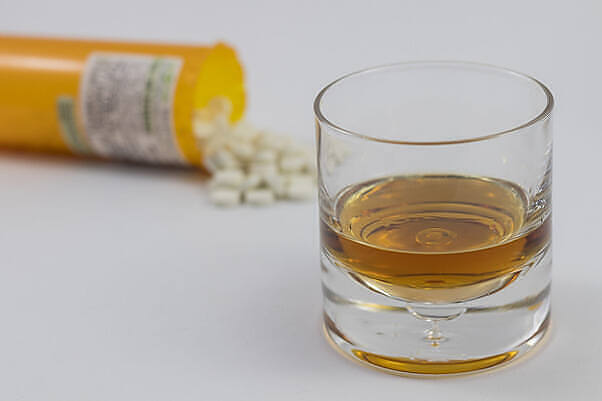 Glass of alcohol next to spilled prescription pills, illustrating risks of combining alcohol with medications