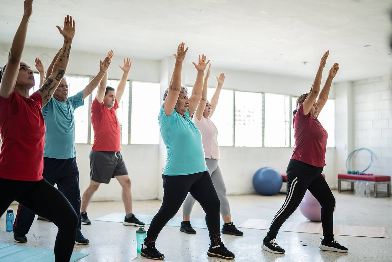 Diverse group of people participating in a fitness class as part of alcohol rehabilitation program, with arms raised in a bright, spacious room