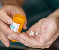 Hands holding a prescription pill bottle and several white tablets, illustrating medication management for Bromazepam addiction treatment