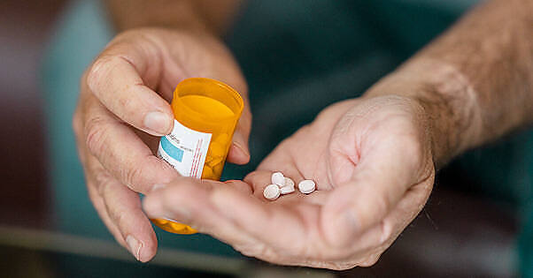 Hands holding a prescription pill bottle and several white tablets, illustrating medication management for Bromazepam addiction treatment