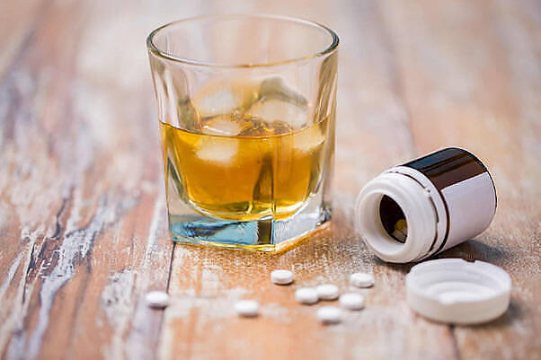 Glass of whiskey on ice next to an open pill bottle with scattered white tablets, illustrating the hazardous combination of benzodiazepines and alcohol