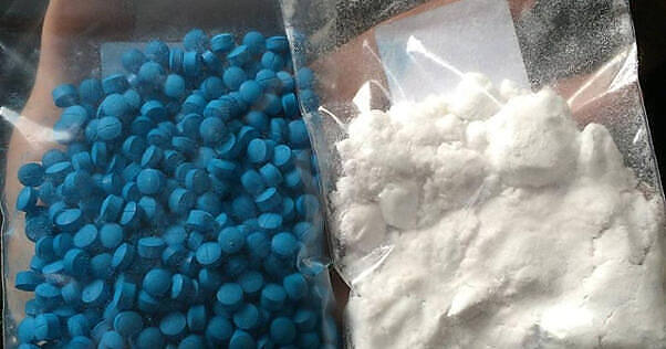 Two plastic bags containing dangerous drugs - one filled with blue pills, likely ecstasy or fentanyl, and another with white powder, possibly cocaine or methamphetamine