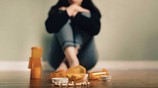 Person sitting on floor with prescription bottles and pills scattered in foreground, symbolizing struggle with Klonopin addiction and need for professional help