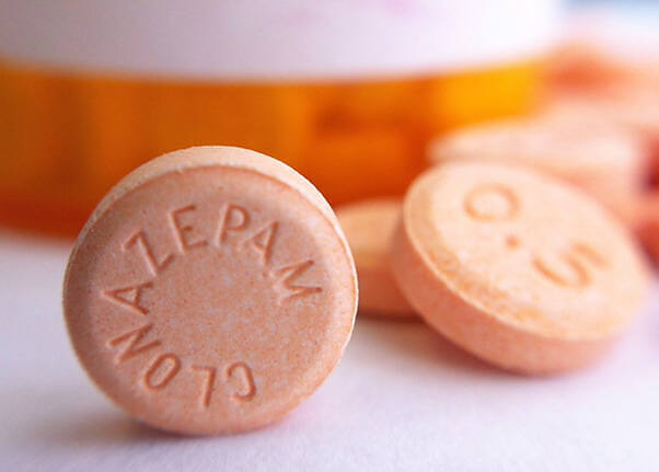 Close-up of Klonopin (clonazepam) tablets, showing the imprinted text 'CLONAZEPAM' on orange pills next to a prescription bottle