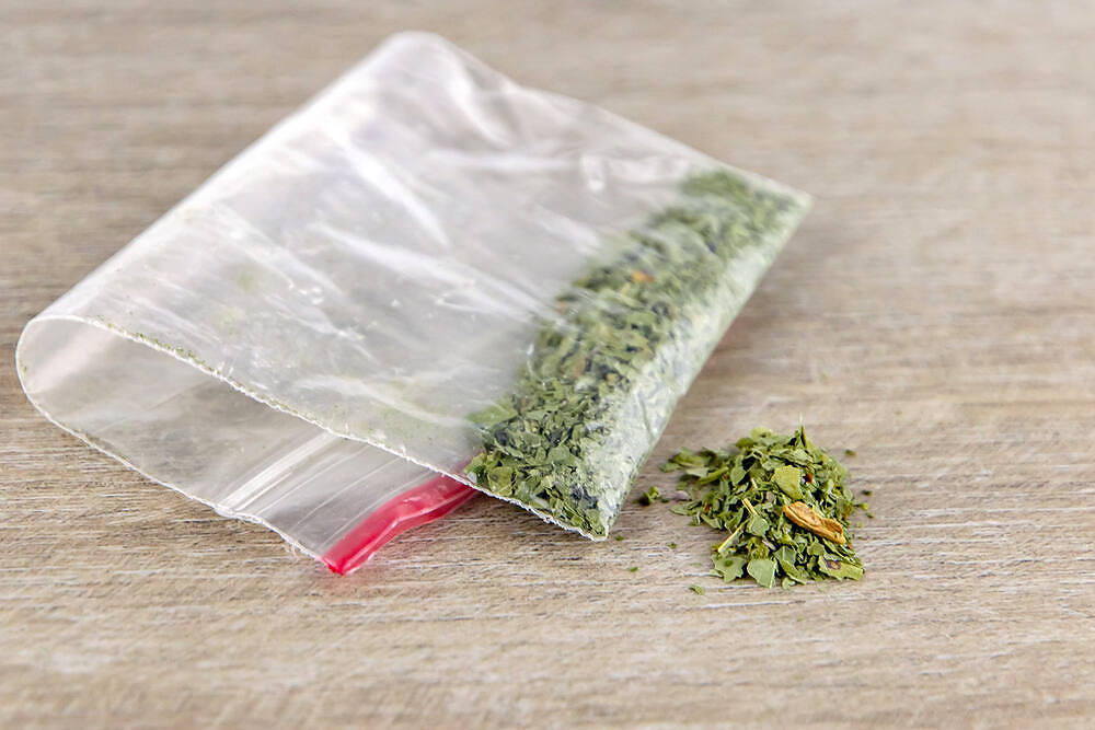 Small plastic bag containing dried marijuana leaves on wooden surface, illustrating cannabis possession and use