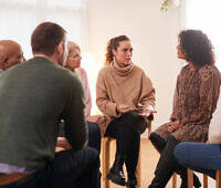 Diverse group of people sitting in a circle during a therapy session, focused on a woman speaking in the center