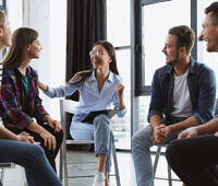 Diverse group of young adults engaged in a supportive therapy session, smiling and interacting positively