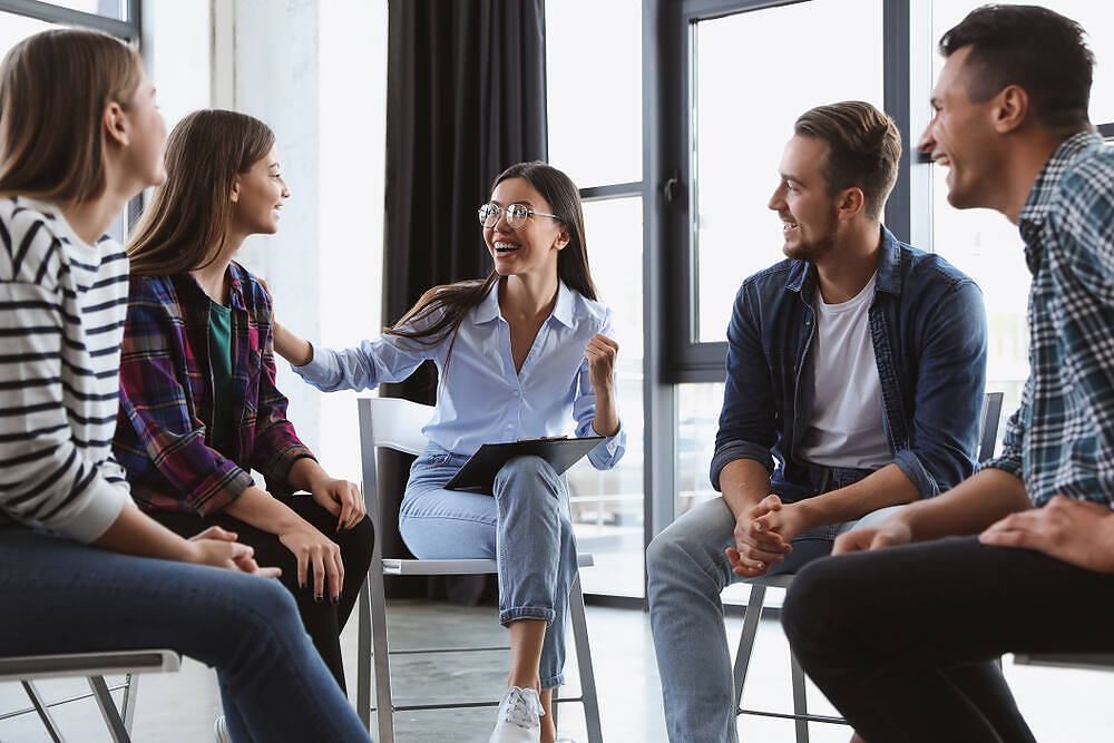 Diverse group of young adults engaged in a supportive therapy session, smiling and interacting positively