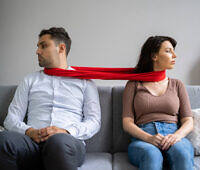 Couple sitting apart on couch, connected by red scarf, symbolizing relationship tension due to addiction