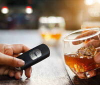 Hand holding glass of whiskey next to another hand with car key fob, illustrating risks of drunk driving