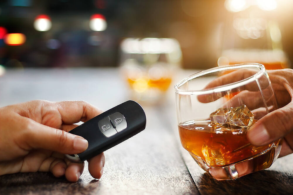 Hand holding glass of whiskey next to another hand with car key fob, illustrating risks of drunk driving