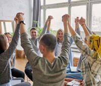 Diverse group of people in a therapy circle raising joined hands, showing unity and support in addiction recovery