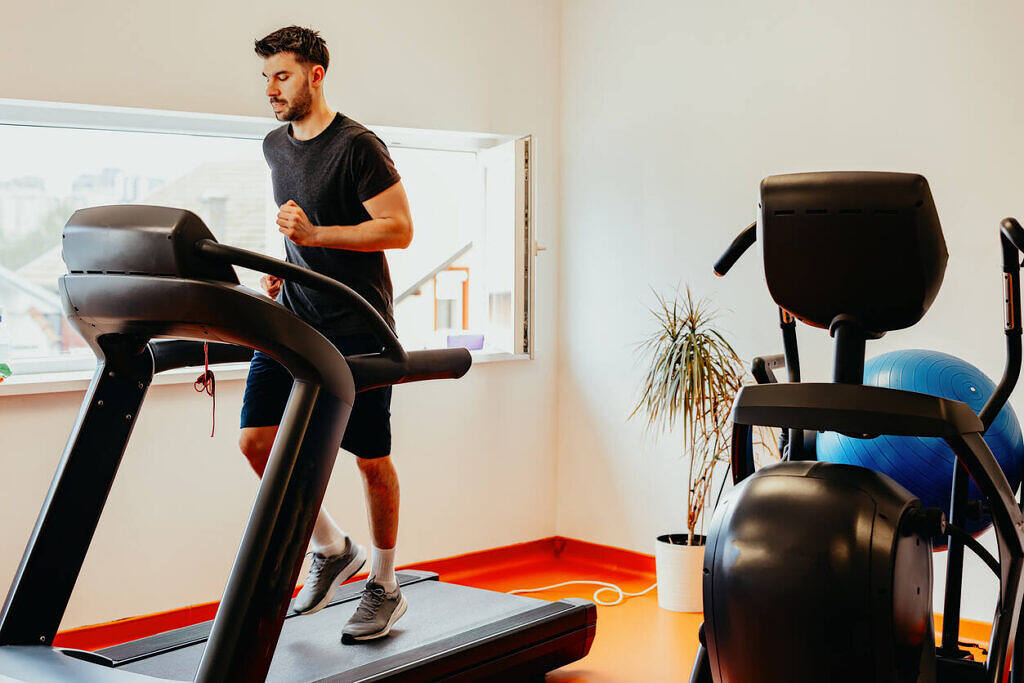 Man exercising on a treadmill in a well-equipped, bright rehab facility gym with modern fitness equipment