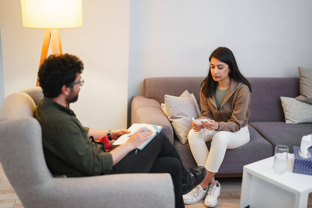 Therapist conducting an initial assessment with a client in a comfortable rehab setting, demonstrating the first step of rehabilitation