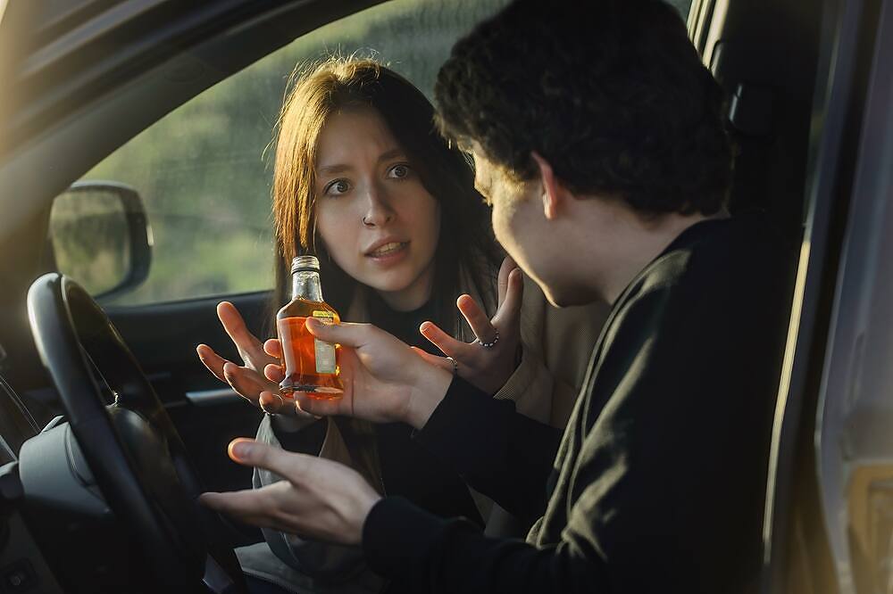 a man holding a bottle of alcohol in a car