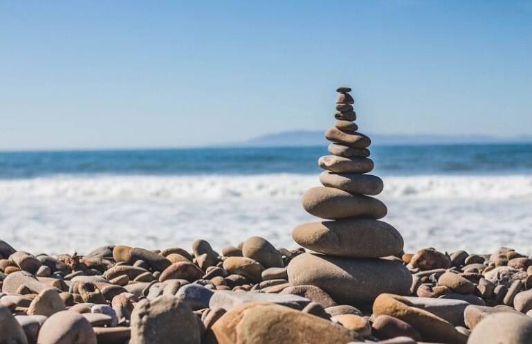 Stack of balanced stones on a beach with ocean waves in the background, symbolizing the balance and harmony achieved in addiction recovery