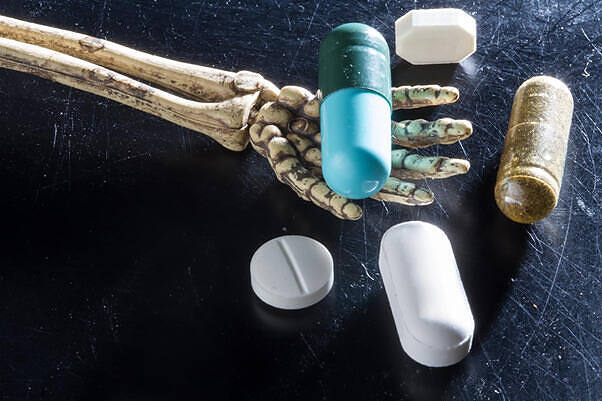 Skeletal hand holding colorful pills and capsules, illustrating the dangers of drug abuse and addiction