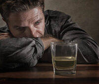 Depressed man staring at a glass of alcohol, illustrating the challenges of giving up drinking